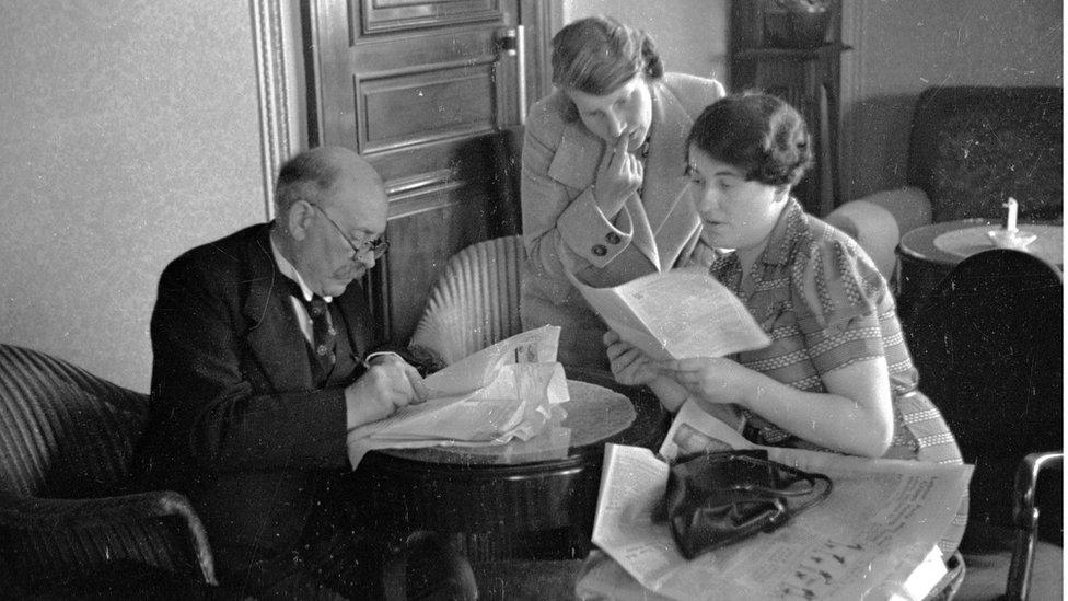 George Dallas wearing glasses sitting at a desk with two women