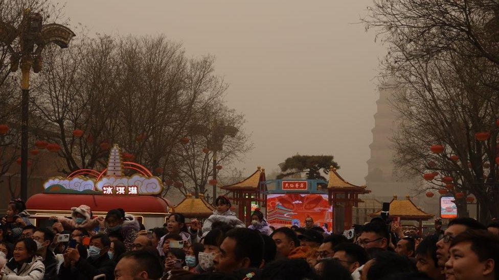 A crowd of people, some wearing masks