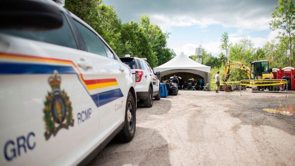 RCMP cars parked at Roxham Road as construction workers install a new light pole in the distance.