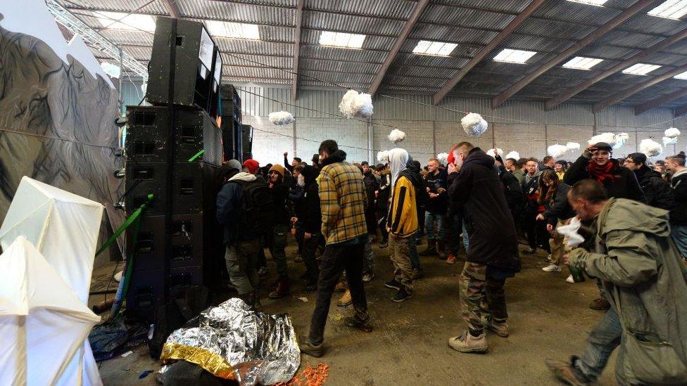 People stand in front of speakers inside the warehouse