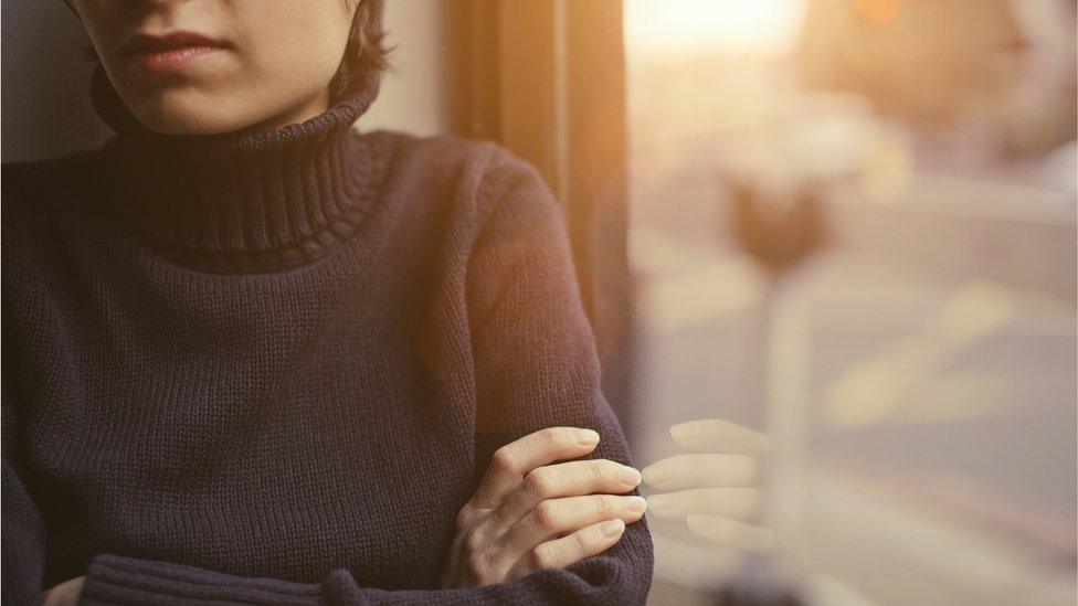 Lone woman stood by window with arms folded