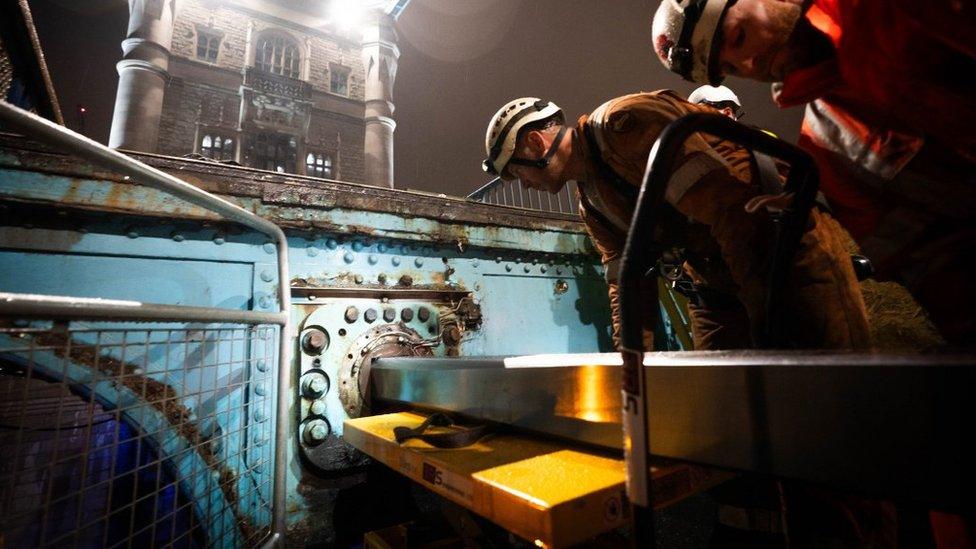 Two engineers handle a massive bolt inside the blue bridge itself