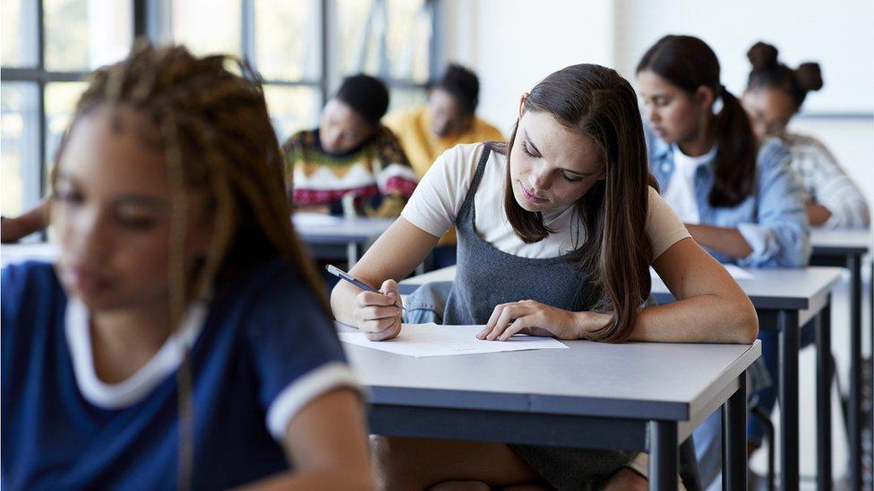 Young multi-ethnic female students writing exam while sitting at desk in examination hall