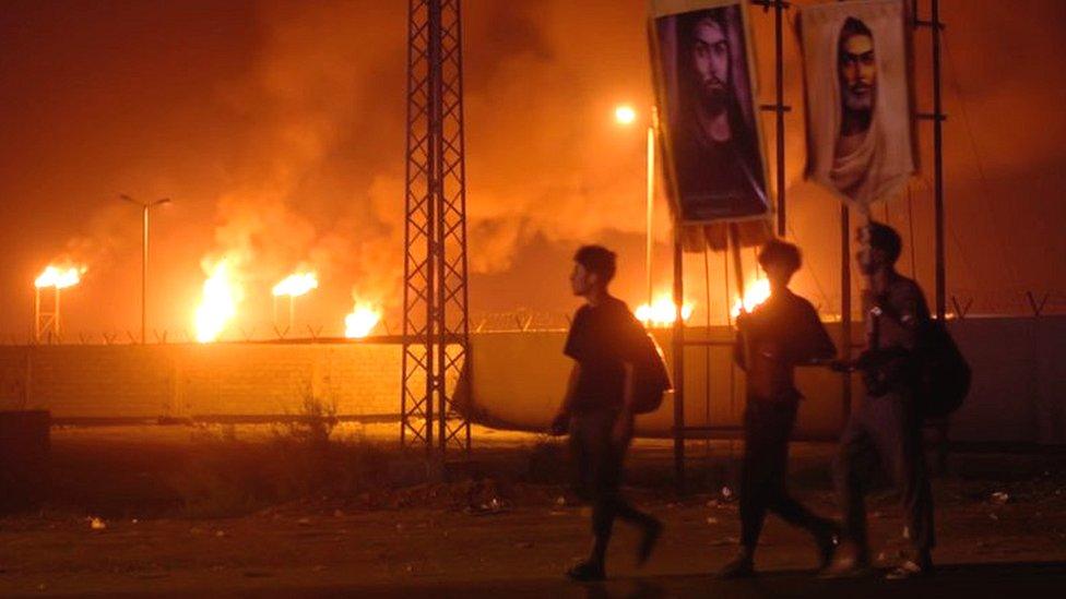 Three young men walk past flares in the Gulf
