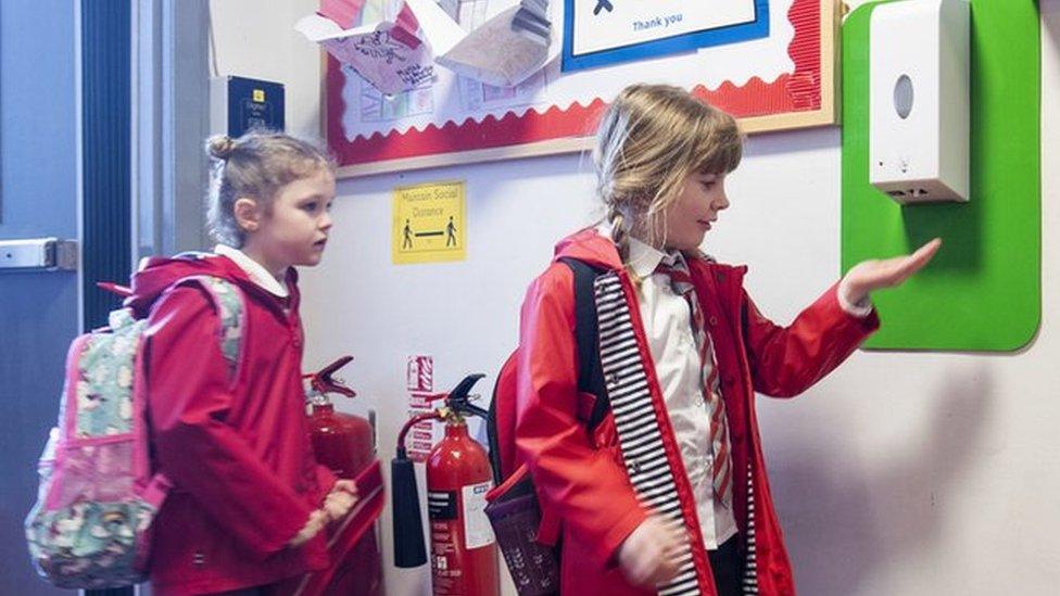 Children sanitise their hands on their way into school