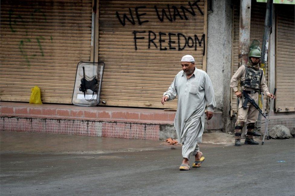 An Indian paramilitary soldier looks on as a Kashmiri pedestrian walks during curfew in Srinagar on August 25, 2016.