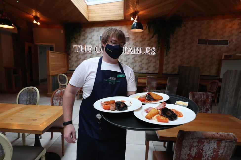 A waiter wearing a face mask carries a tray of three breakfast meals