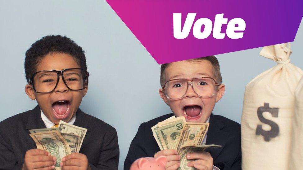 two young boys in glasses, holding up dollars, with bags on money on the table and lots of dollar notes in front of them.