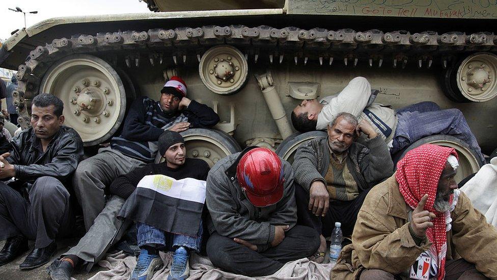 Protesters huddle beside the tracks of a tank in Cairo (06/02/11)