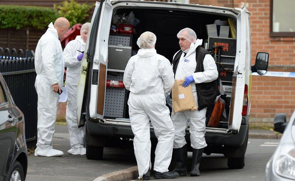 Investigators in white overalls behind an open van