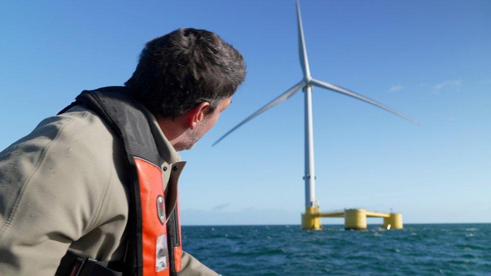 Climate editor Justin Rowlatt in foreground looking at a floating turbine in the background