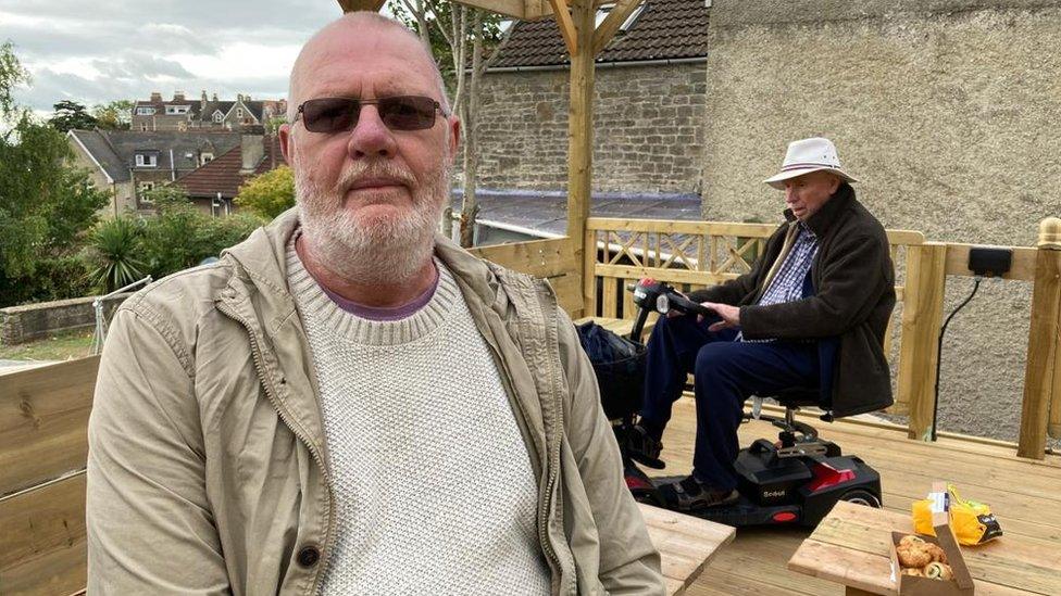 Mike Somerton sitting in the rebuilt shed, with a man on a mobility scooter behind him