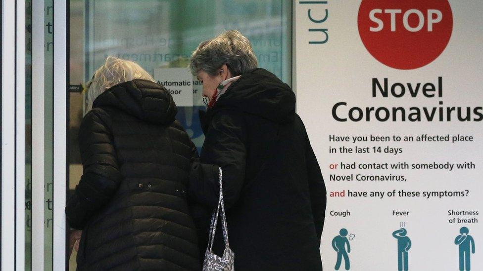 Two women walk past a sign providing guidance information about novel coronavirus (COVID-19) at one of the entrances to University College Hospital in London on March 5, 2020. - The number of confirmed cases of novel coronavirus COVID-19 in the UK rose to 85 on March 4, with fears over the outbreak delaying the global release of the new James Bond movie and causing lack of demand for air travel that has proved the final nail in the coffin for British regional airline Flybe which went into administration on March 5.