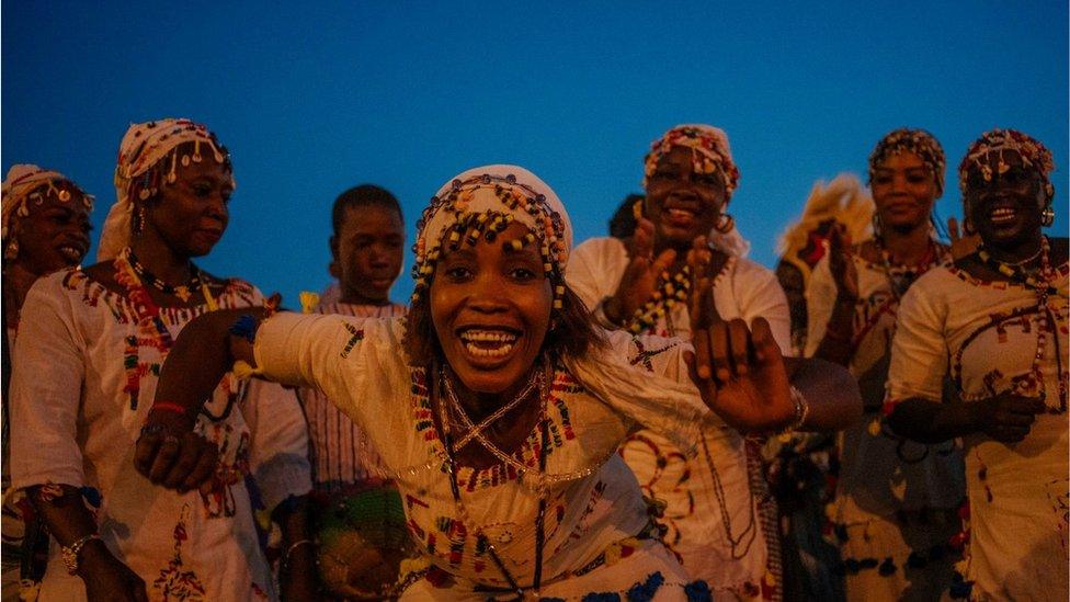 Women dancing dressed in white with beaded head dresses. The woman in the middle is dancing and smiling