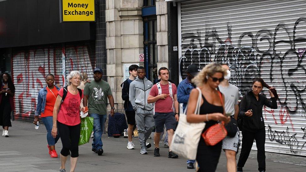 People walking past shops with shutters down in London