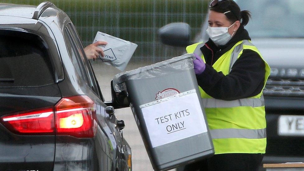 A motorist drops off a testing kit to a staff members wearing a protective face mask at an NHS coronavirus self-test site outside London's 02 arena