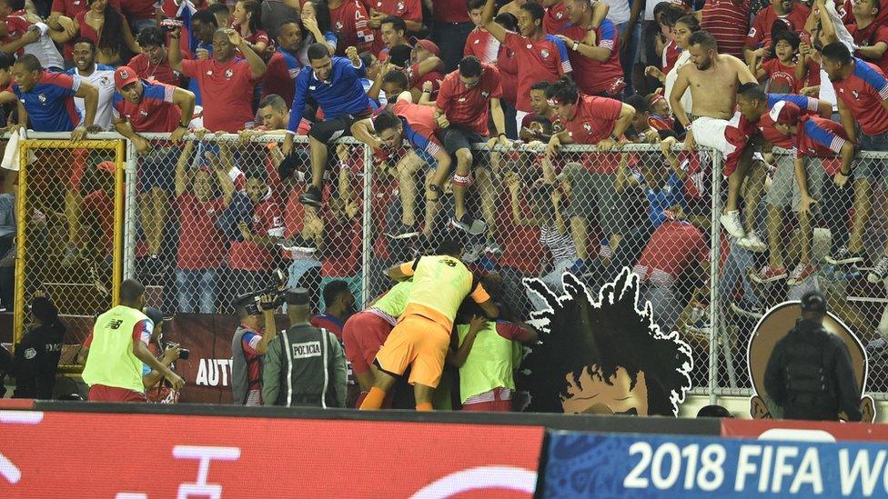 Panama fans clamber over fences separating them from the football pitch as the Panama team celebrates below.