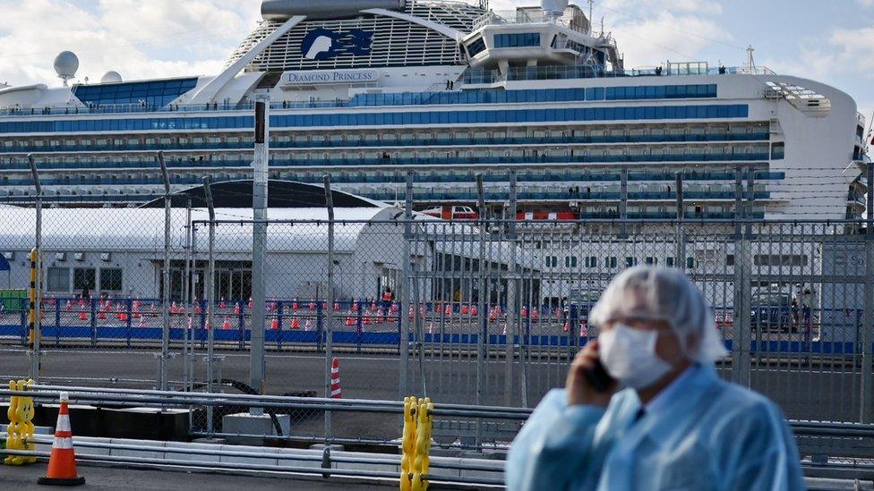 A man in protective gear speaks on the phone near the Diamond Princess cruise ship in quarantine due to fears of the new COVID-19 coronavirus, at the Daikoku Pier Cruise Terminal in Yokohama on February 19, 2020