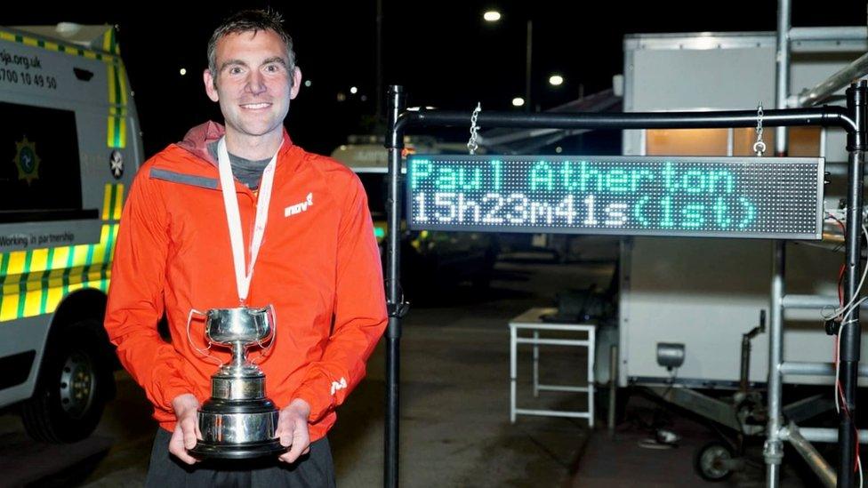 Paul Atherton holding the trophy with his finishing time on a board behind him