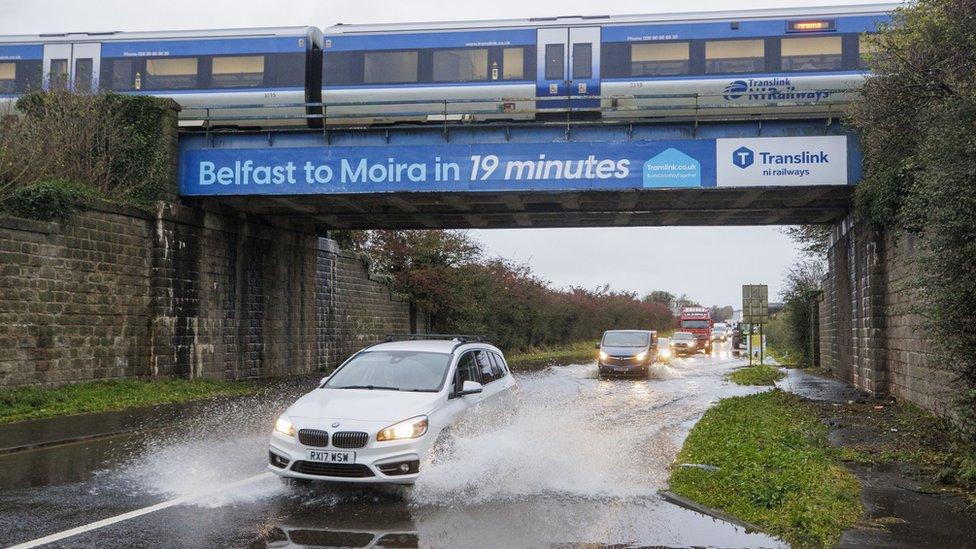 A car moves through a deep water on a road near Moira in County Down as a train crosses a bridge overhead