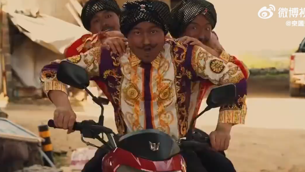 A screengrab from the video showing three men in blackface on a motorbike