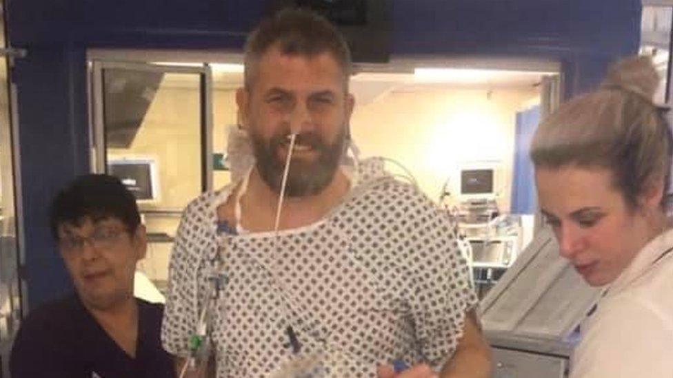 Stuart Cock in hospital gown with two members of hospital staff