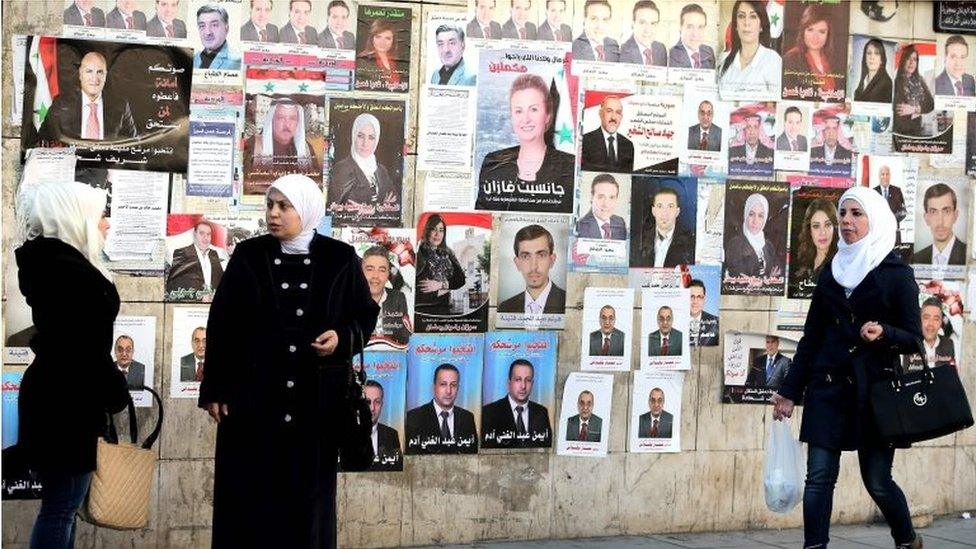 Women in front of wall of election campaign posters in Damascus (02/04/16)