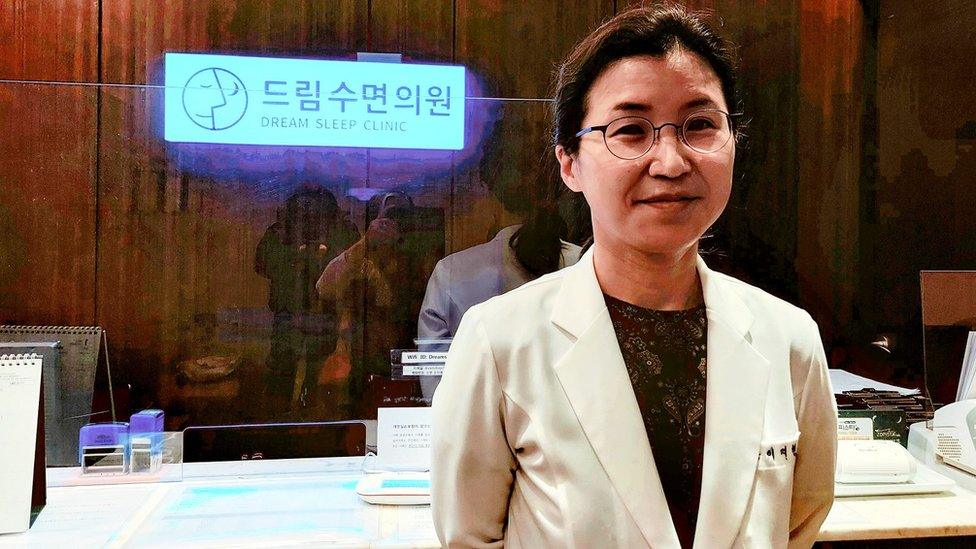 Female doctor stands in front of a reception desk with the sign Dream Sleep Clinic glowing in the background