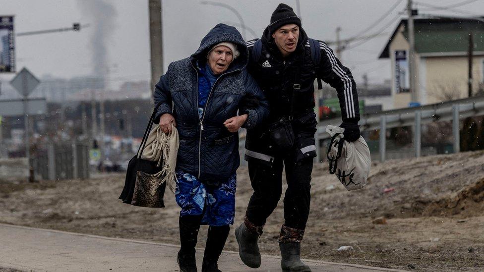 A man helps an elderly woman to run for cover in Irpin, near Kyiv