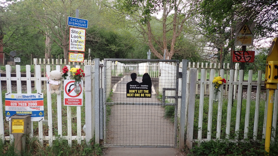 A railway crossing, with warning signs and tribute flowers