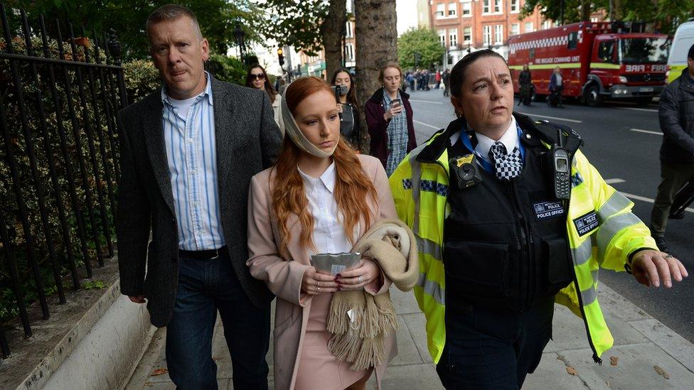 A female casualty is led from the scene by a police officer