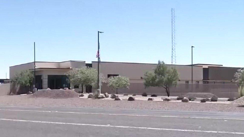 A grey, low building sits on a nondescript highway under a hot sun in this photo