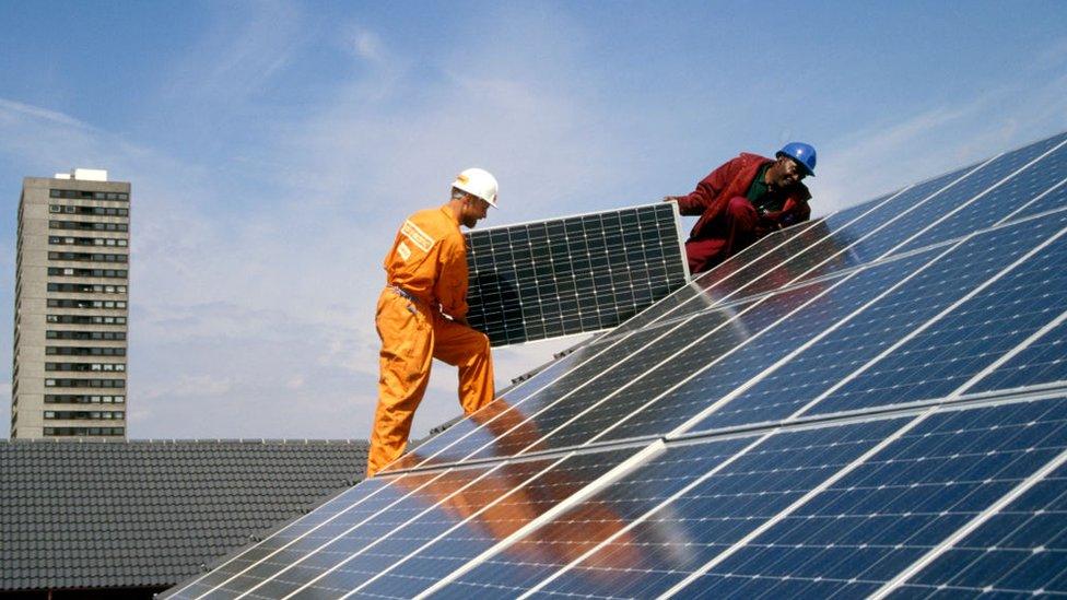 Engineers fitting solar panels to a roof at Silvertown Solar Village, Docklands, London UK