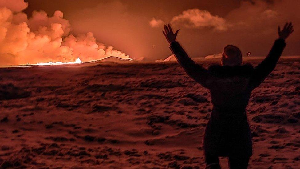 A local resident watch smoke billow as the lava colour the night sky orange from an volcanic eruption on the Reykjanes peninsula 3 km north of Grindavik, western Iceland on December 18, 2023.