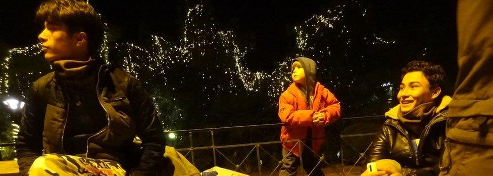 Migrants sit surrounded by Christmas lights