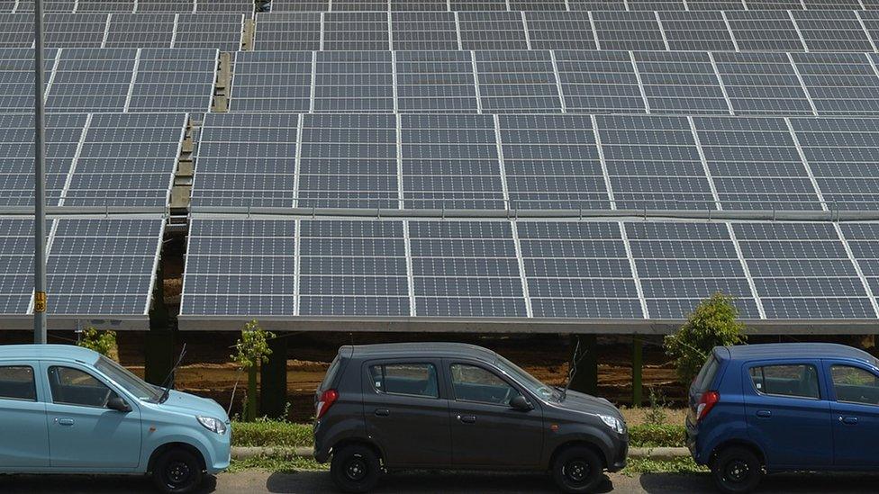 Newly finished cars stand next to solar panels at a solar power plant built on the site of Indian vehicle manufacturer Maruti Suzuki at Manesar on the outskirts of New Delhi on June 3, 2014.