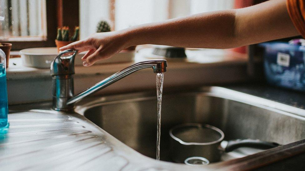 Hand reaching across a sink below a window,