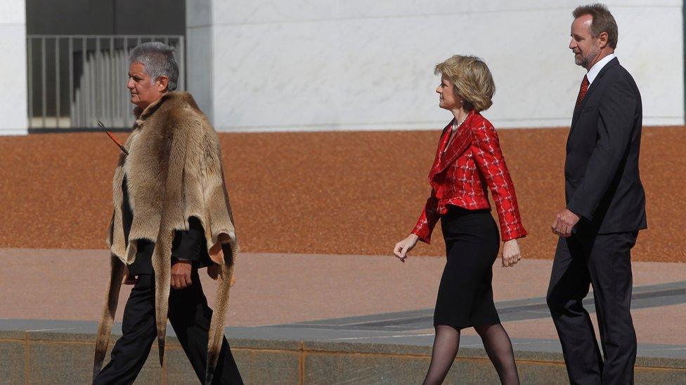 Ken Wyatt wearing a traditional Indigenous kangaroo skin coat walks in front of Liberal MPs Julie Bishop and Nigel Scullion outside parliament house in 2010