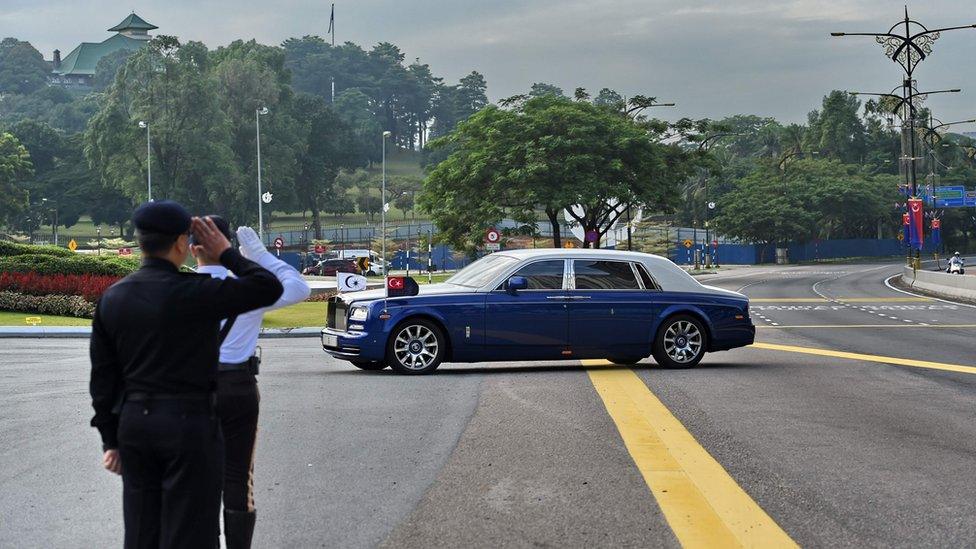 Policemen salute as a Rolls-Royce belonging to the Sultan of Johor enters the Istana Bukit Serene palace