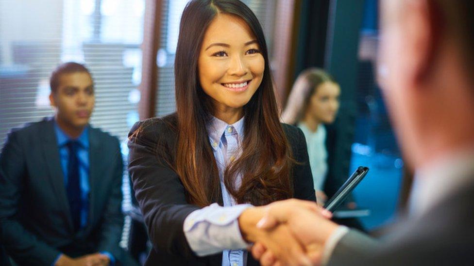 Woman shaking hands with man and woman sat behind