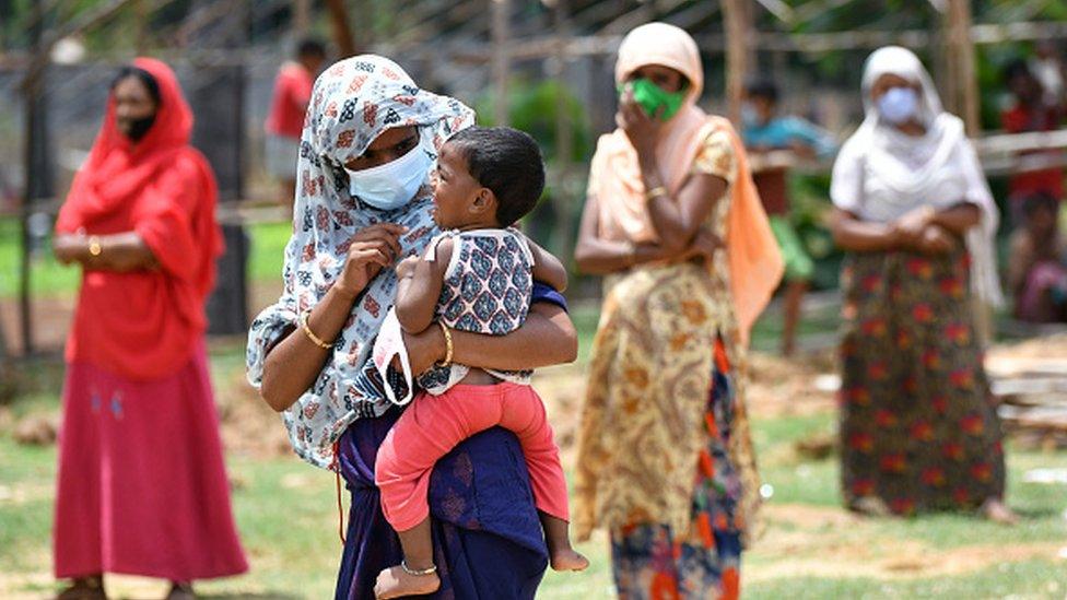 A mother entertains her child while she along with other Rohingya refugees wait in line for ration supplies in their camp in Jakkur in Bangalore