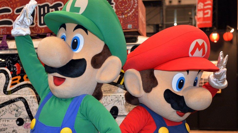 People wave, dressed in costumes as Nintendo characters Mario and Luigi