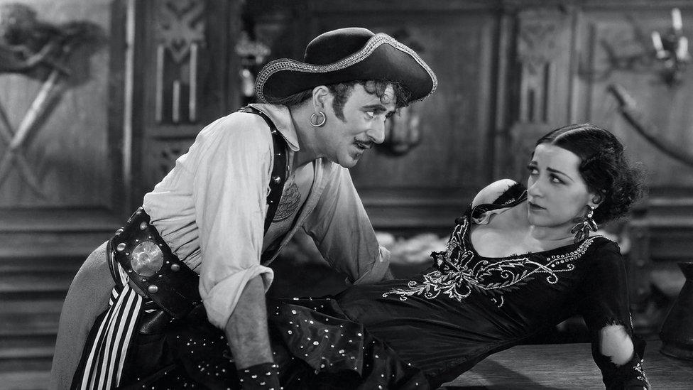 A still from a 1920s pirate film showing a male pirate menacing a woman