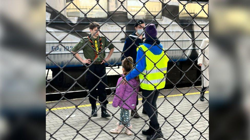 A train guard and a Polish scout help a lost little girl on the platform