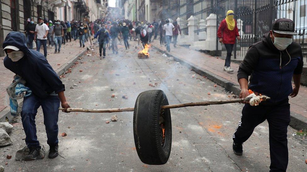 Protesters carry a burning tyre down a road strewn with rocks