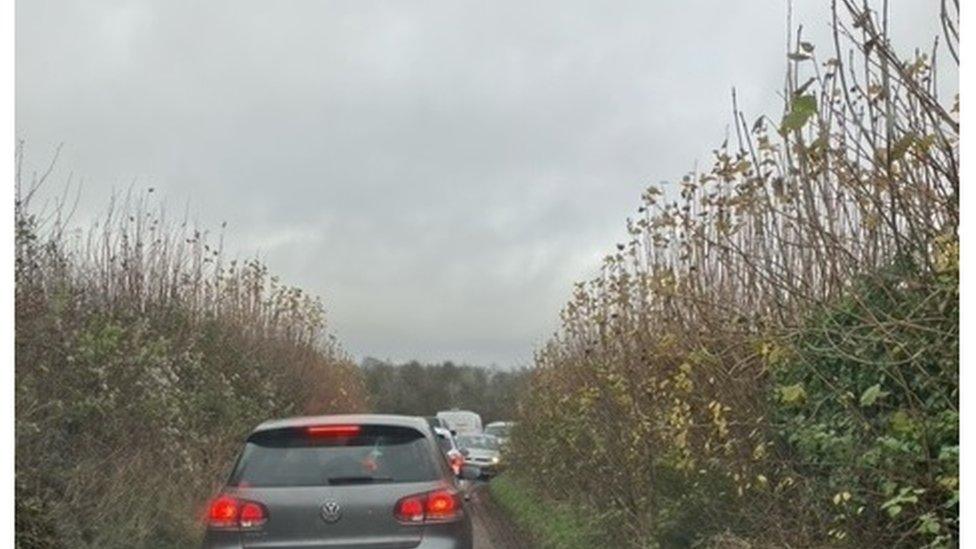 A narrow country single-track lane with cars stuck coming form both directions