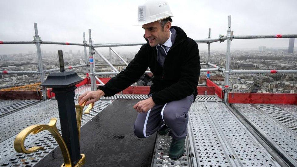 French President Emmanuel Macron touches the cross installed at the top of the spire of Notre Dame de Paris cathedral as restoration work continues in Paris, France, 08 December 2023