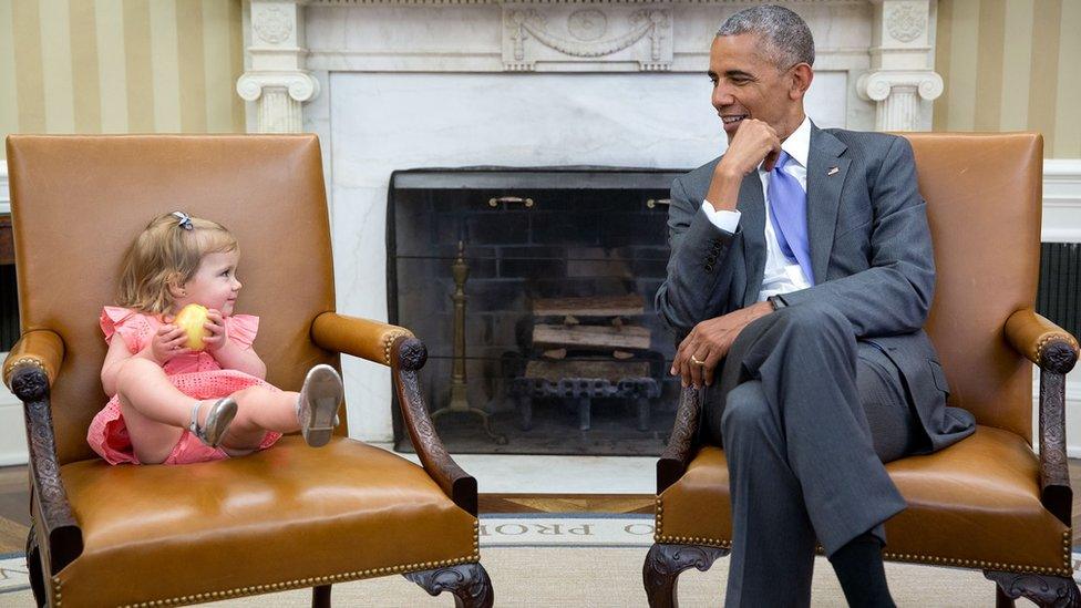 Two matching chairs hold a very young girl in pink, left, and Obama, right, as they share a glance in the White House.