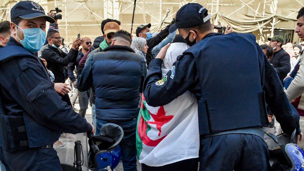 A security forces member embraces a woman draped in an Algerian flag during a student-led demonstration in Algeria's capital Algiers on March 16, 2021.