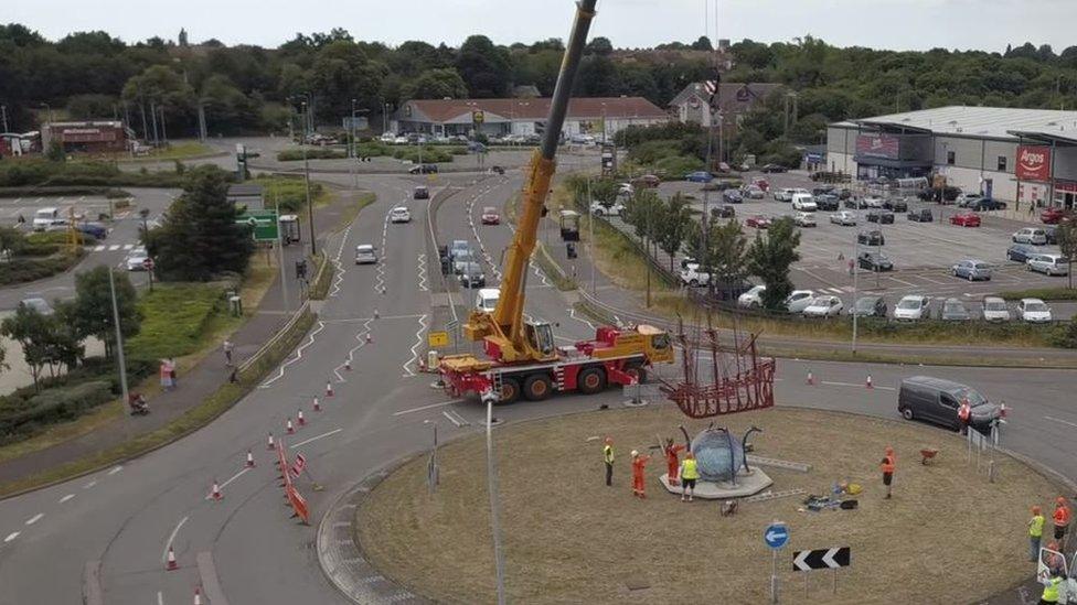 The crane lowers the sculpture